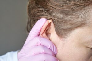 close up of female adult with caucasian skin having ear examined by doctor wearing pink gloves photo